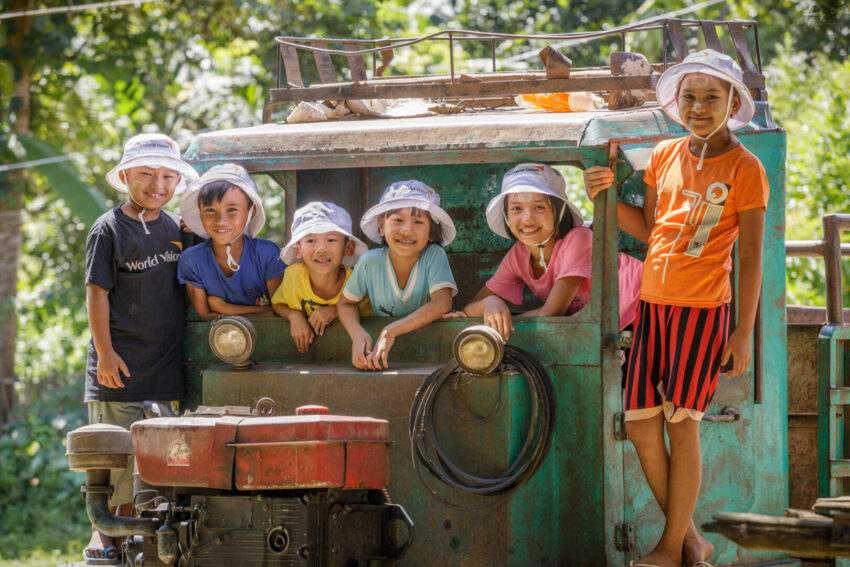 Six smiling children in Myanmar pose for a photo on an old green truck.